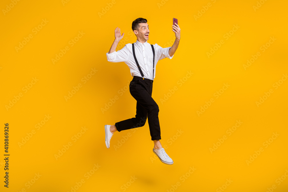 Full length body size photo of jumping man taking selfie waving hand video call isolated on vibrant yellow color background