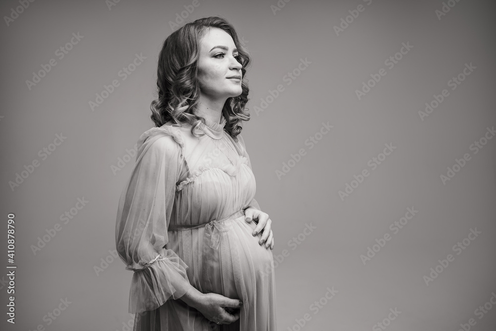 A pregnant girl is holding her belly. A young mother is expecting the birth of a child. The woman gently hugs her baby in the stomach. Black and white photo of a pregnant girl