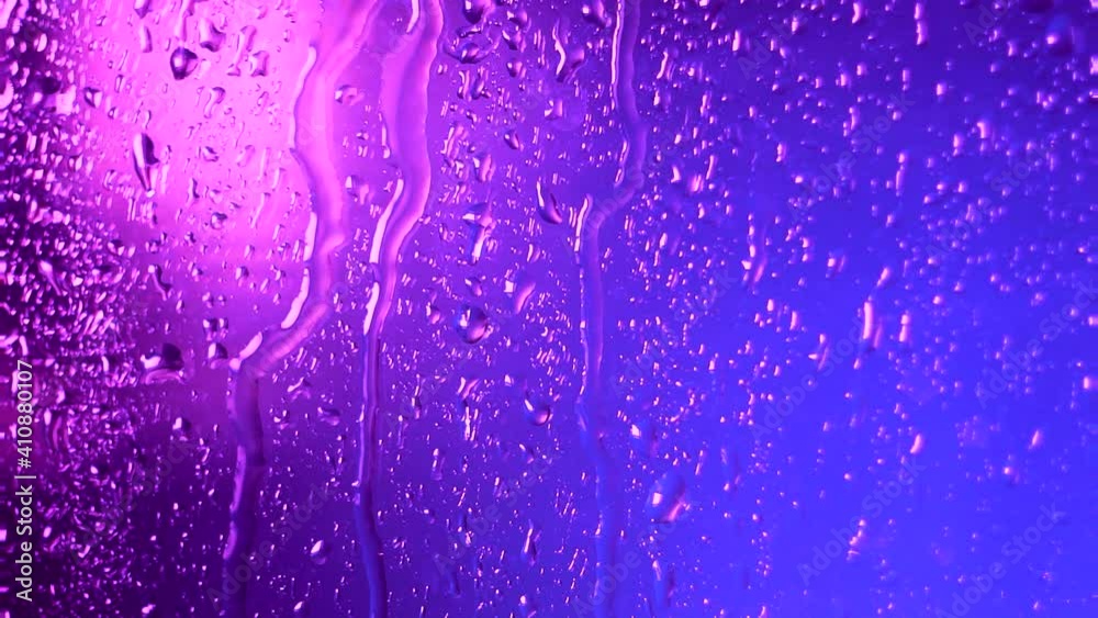 Raindrops of water flow down the glass in rainy weather on a colored pink blue blurred background. Texture and effect of rain on the window