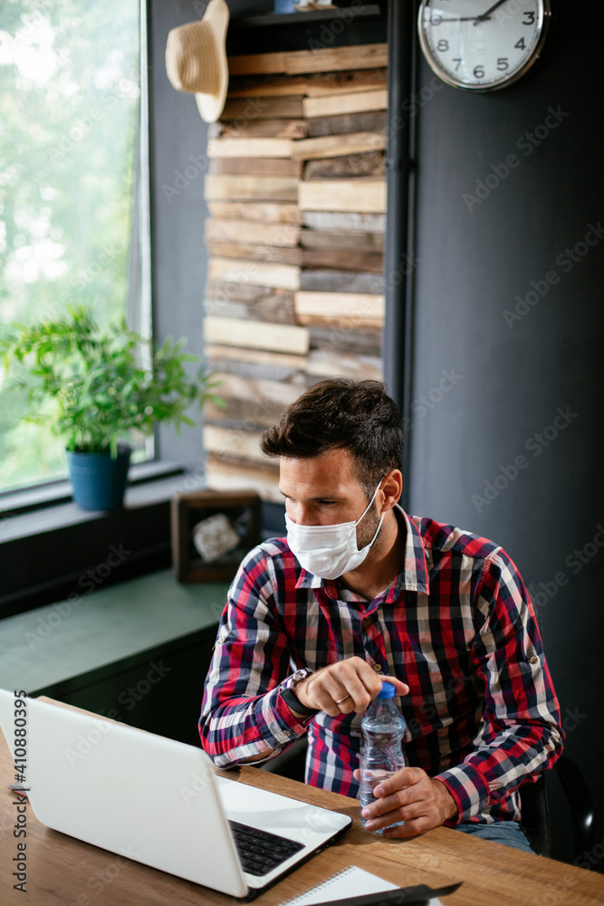 Fototapeta premium Young businessman with a mask working in his office on laptop. COVID - 19 virus protection..