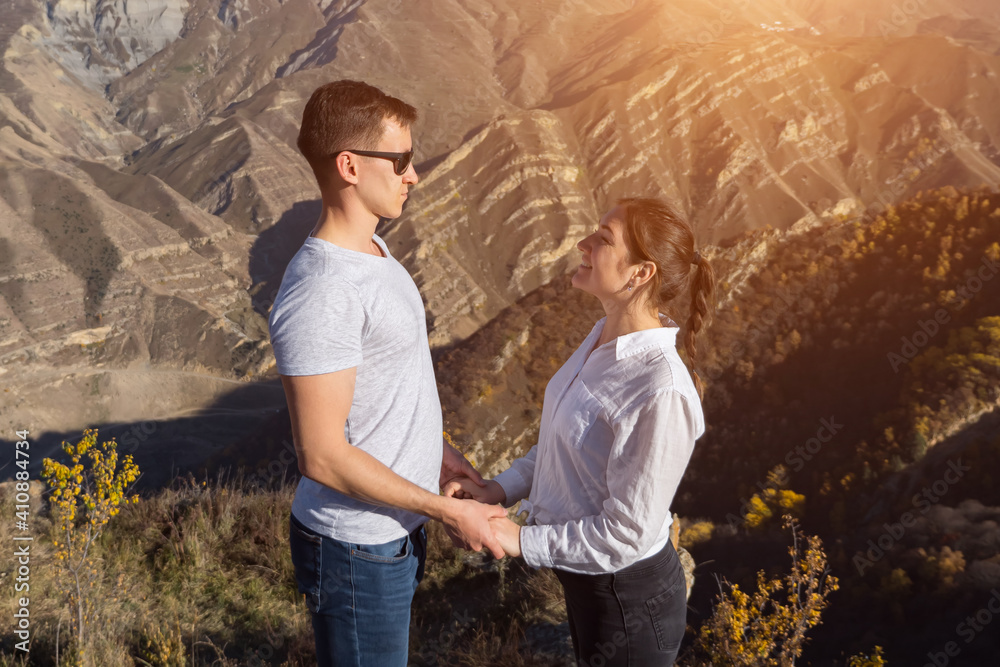 man and a woman stand opposite each other holding hands on the background of mountains, sunlight. man and a woman stand opposite each other holding hands on the background of mountains, sunlight.