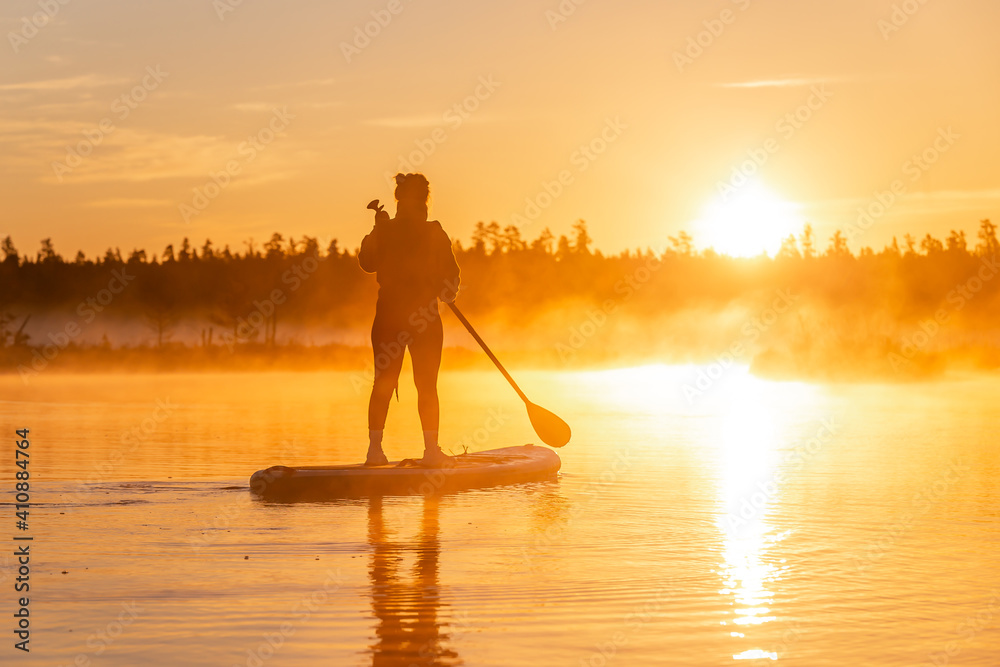 Silhouette of Young asian woman doing SUP stand up paddle boarding at sunrise in lake. Early summer morning activity