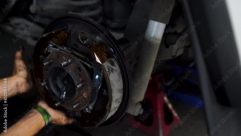 A car mechanic repairing the brakes. Car brake repairing in garage. Car wheel brake disc and shoes of lifted automobile at repair service station. A car mechanic repairing the brakes. Car brake repairing in garage. Car wheel brake disc and shoes of lifted automobile at repair service station.