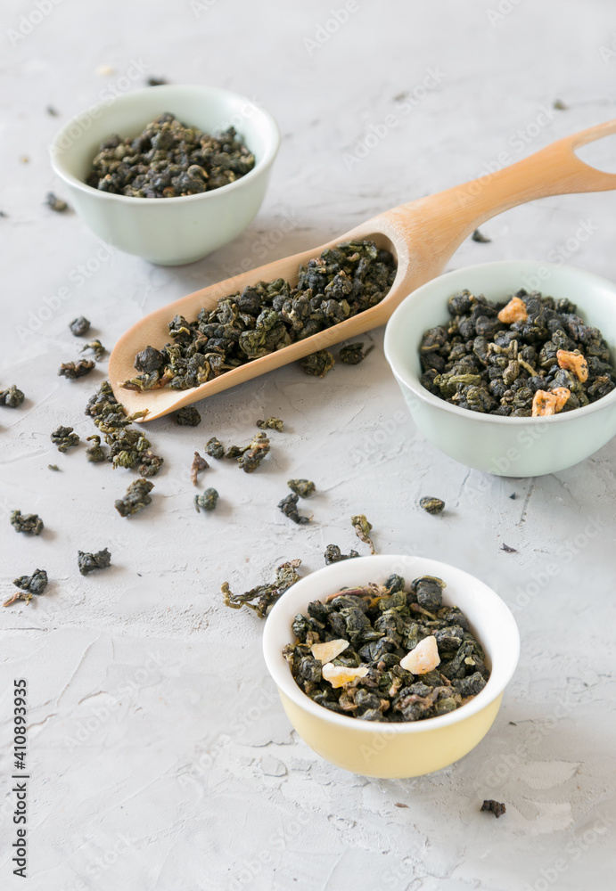 Different varieties of green tea in bowls and measuring spoon on gray background Different varieties of green tea in bowls and measuring spoon on gray background