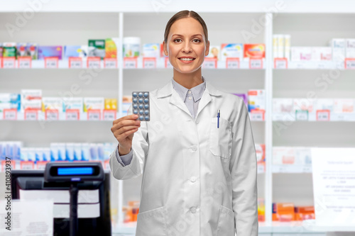 medicine  profession and healthcare concept - happy smiling female doctor or pharmacist holding pills over pharmacy on background