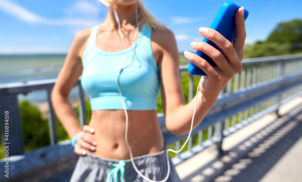 Fototapeta premium sport, fitness and technology concept - close up of happy smiling sporty young woman with smartphone and earphones