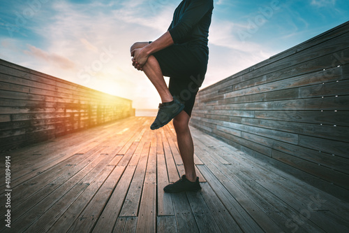 Sporty man warming up and stretching legs before workout outdoors at sunset or sunrise. Stretching gluteus maximus muscle. Athletic man doing fitness stretching exercises. Sport and healthy lifestyle