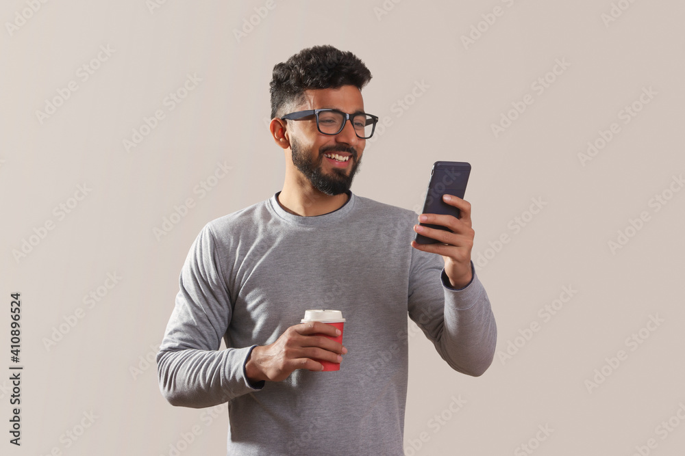 Young man looking at his phone and holding a coffee cup. Young man looking at his phone and holding a coffee cup.