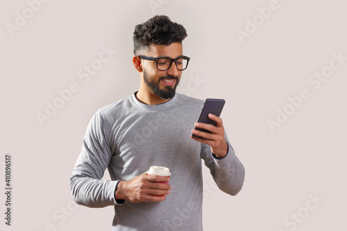 Young man looking at his phone and holding a coffee cup. 	