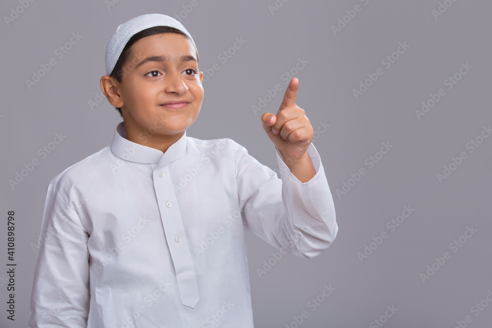 Young Muslim boy wearing cap looking away, smiling and pointing Young Muslim boy wearing cap looking away, smiling and pointing