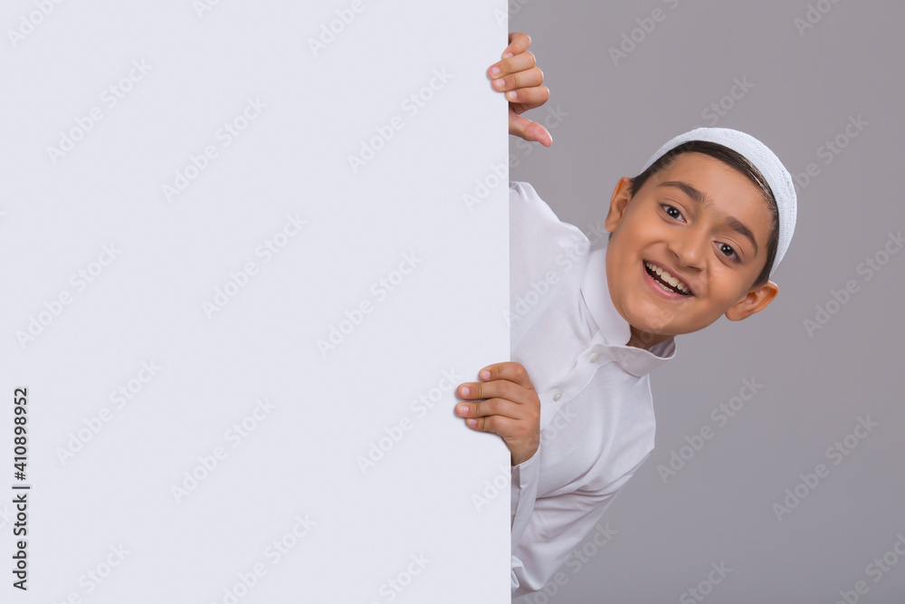 Young Muslim boy wearing cap peeking out from behind the wall Young Muslim boy wearing cap peeking out from behind the wall