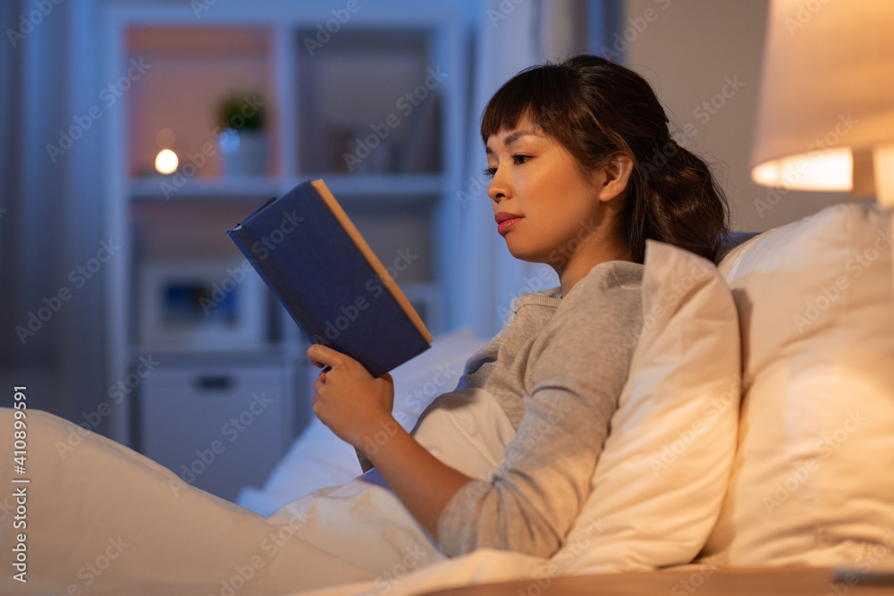 © Syda Productions - people, bedtime and rest concept - young asian woman reading book in bed at home at night