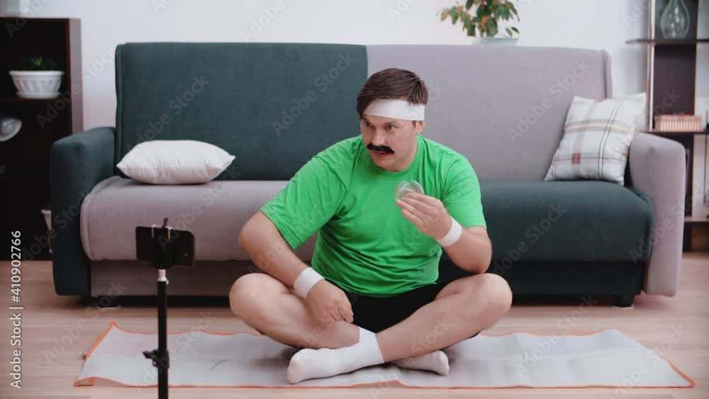 A funny male athlete sits on the floor looks at a smartphone and turns a spinet. Beauty and sports concept.