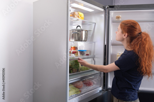 Woman standing at the open refrigerator with fruits, vegetables and healthy food