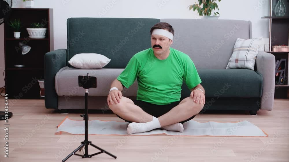 A funny male athlete sits on the floor looking at a smartphone and listens to what he is told on the video. Beauty and sports concept. A funny male athlete sits on the floor looking at a smartphone and listens to what he is told on the video. Beauty and sports concept.