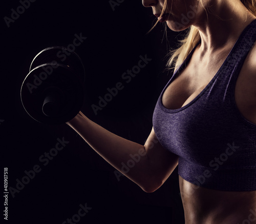 Slim athletic woman Holding dumbbell in the hand on black photo