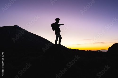 Silhouette of traveler backpacker standing near Mount Teide and showing with hand to the sunset horizon