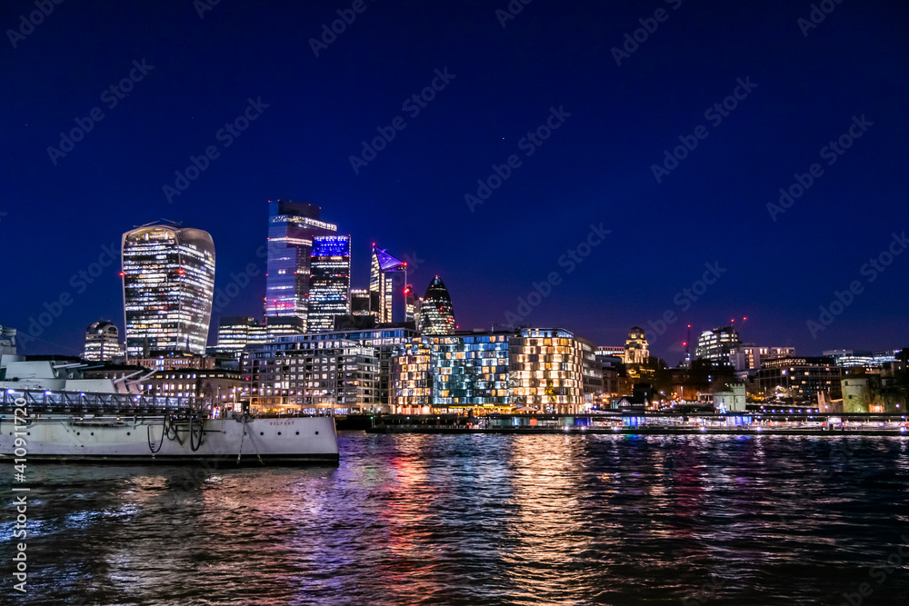 London cityscape at night view at the City of London from across the river Thames, night life in UK capital city, lots of lights and reflections in the water and beautiful sky