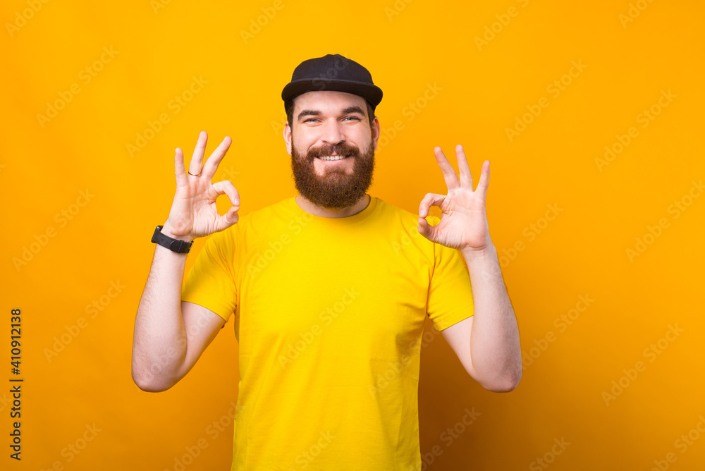 Naklejka premium Photo of joyful young man in yellow shirt showing OK gesture and smiling at camera.