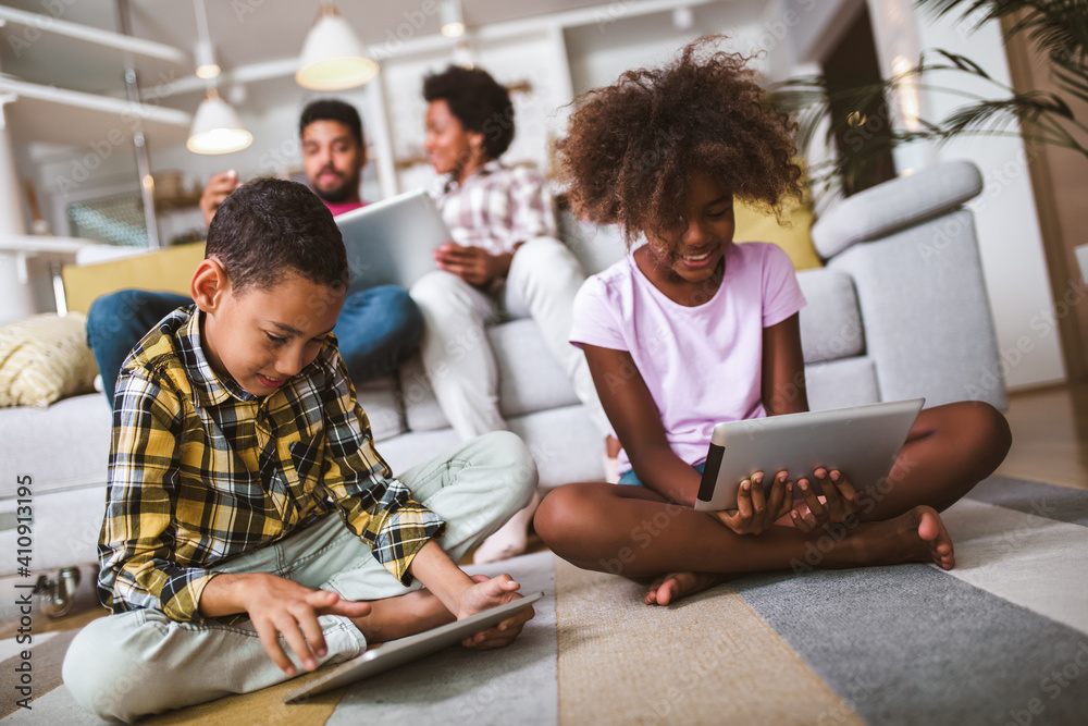 Fototapeta premium African american boy and girl lying on floor and using digital tablet. Family at home.