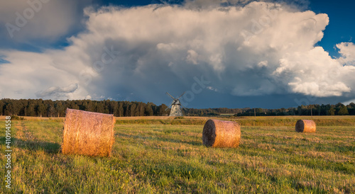 Countryside landscape with rolls of haystack, cumulus clouds and old windmill...