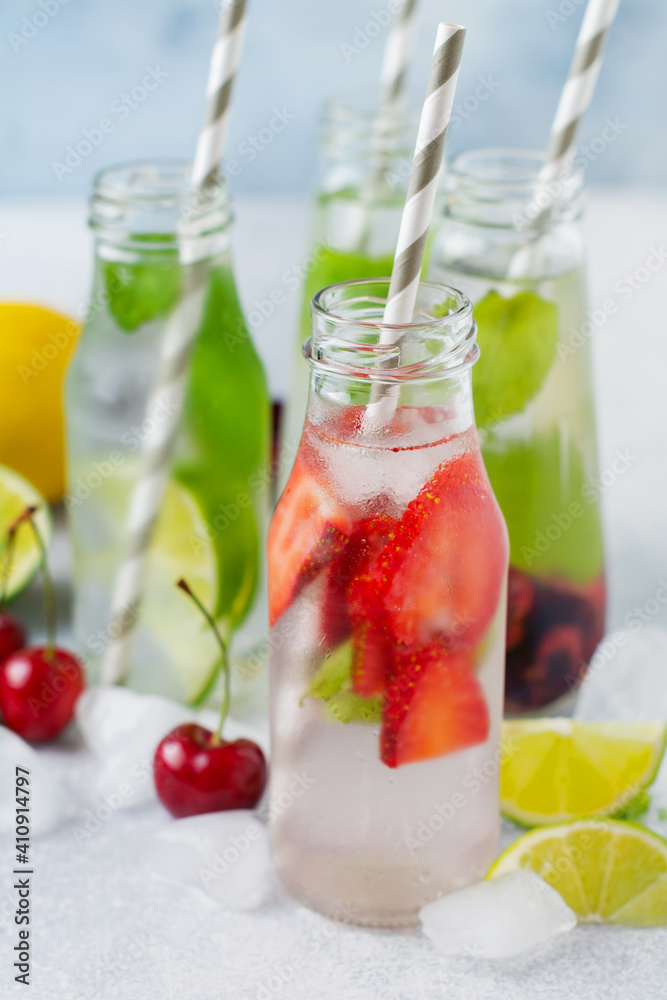 Lots of bottles with refreshing summer lemonade with lime, strawberry, cherry, cucumber and ice on a gray concrete background. Lots of bottles with refreshing summer lemonade with lime, strawberry, cherry, cucumber and ice on a gray concrete background.