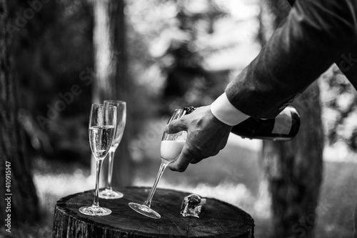 Man hands pouring champagne from a bottle in glass that stand on buffet table. Close up. Black and white photo