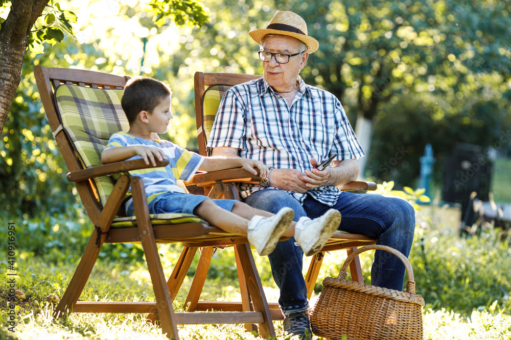 Grandpa sitting with his grandson in the garden. They're talking and joying on a beautiful summer day. Grandpa sitting with his grandson in the garden. They're talking and joying on a beautiful summer day.