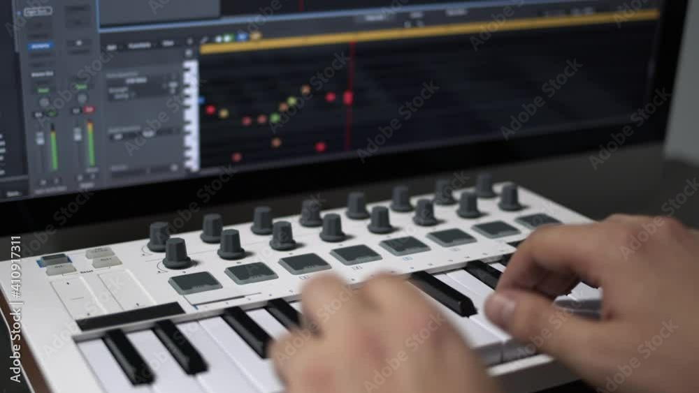 Male hands recording music, playing electronic keyboard, midi keys on the table. Closeup of male hands composing music in sequencer using midi keyboard with keys and pads