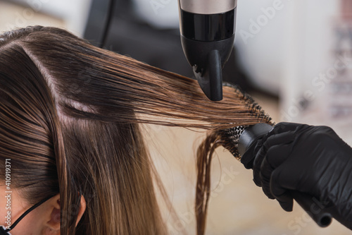 Professional female hairdresser drying woman's hair styling using blow dryer at the hairdressing saloon