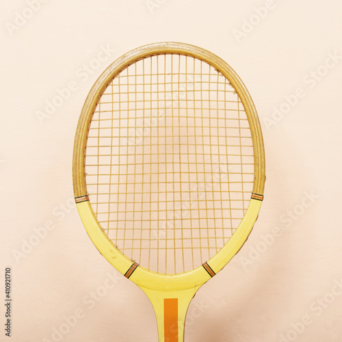 Vintage wooden tennis racket against pink wall, pastel tones of yellow, orange and pink, retro sport concept, square crop