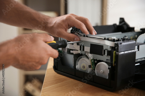 Repairman with screwdriver fixing modern printer indoors, closeup