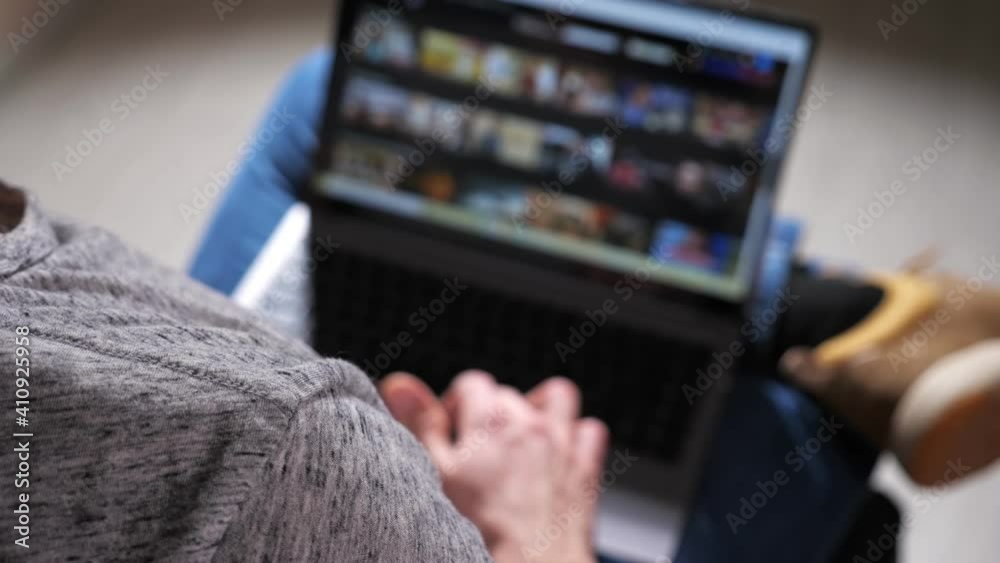 Young white man lying down on sofa in living room at home searching for online films or TV series to watch for fun.