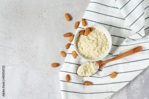almond flour in a bowl and spoon with scattered nuts on a white concrete background