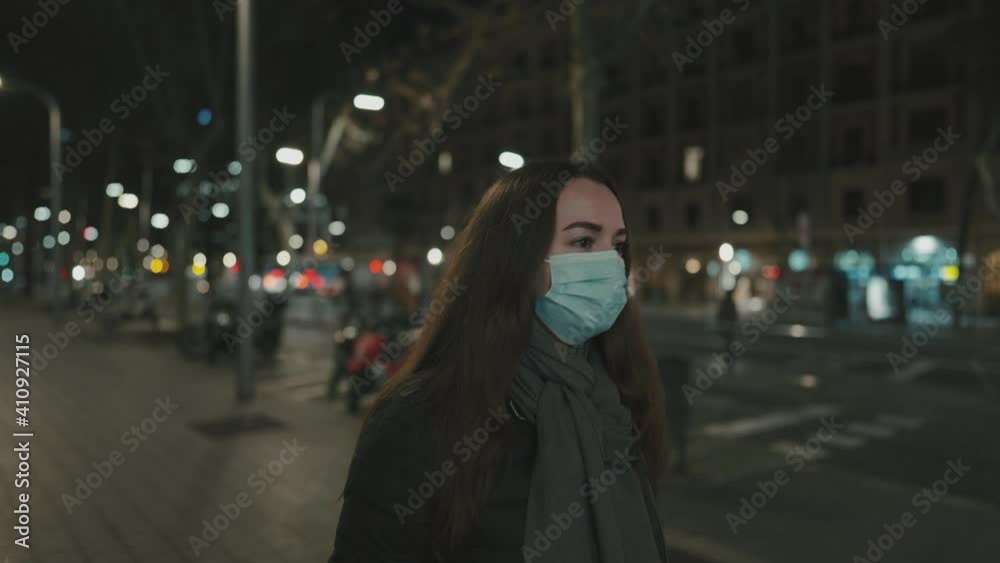 Female model wearing mask against virus, walking alone in the night city street. Background lights of transportation. Coronavirus covid-19 pandemic concept. . Prores 10 bit color space Female model wearing mask against virus, walking alone in the night city street. Background lights of transportation. Coronavirus covid-19 pandemic concept. . Prores 10 bit color space