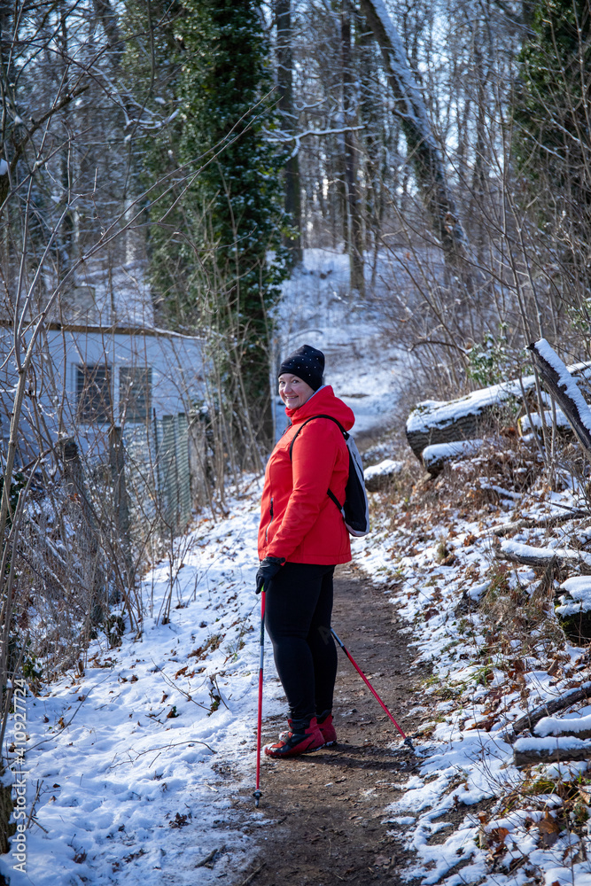 A woman in a red jacket practices Nordic walking in the forest