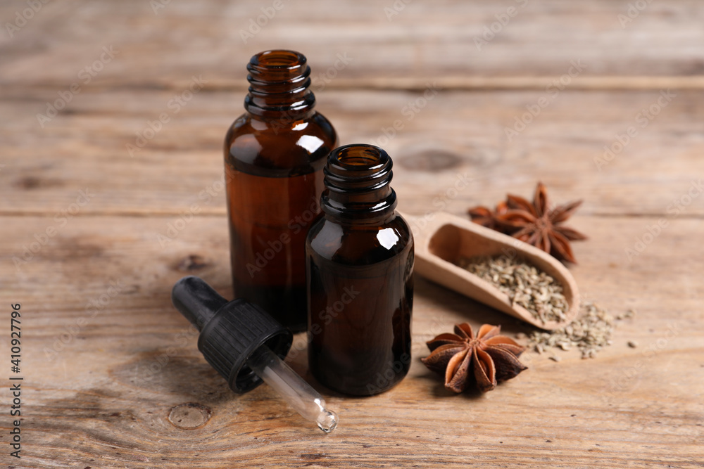 Bottles of essential oil, anise and seeds on wooden table