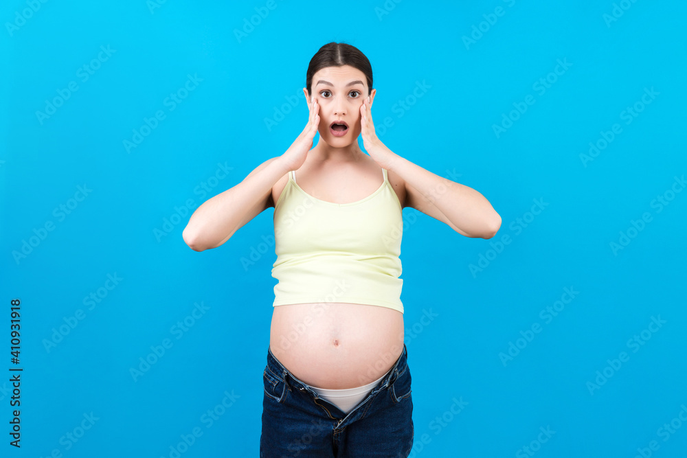 Picture of shocked or surprised pregnant lady standing over colored background. Looking at camera