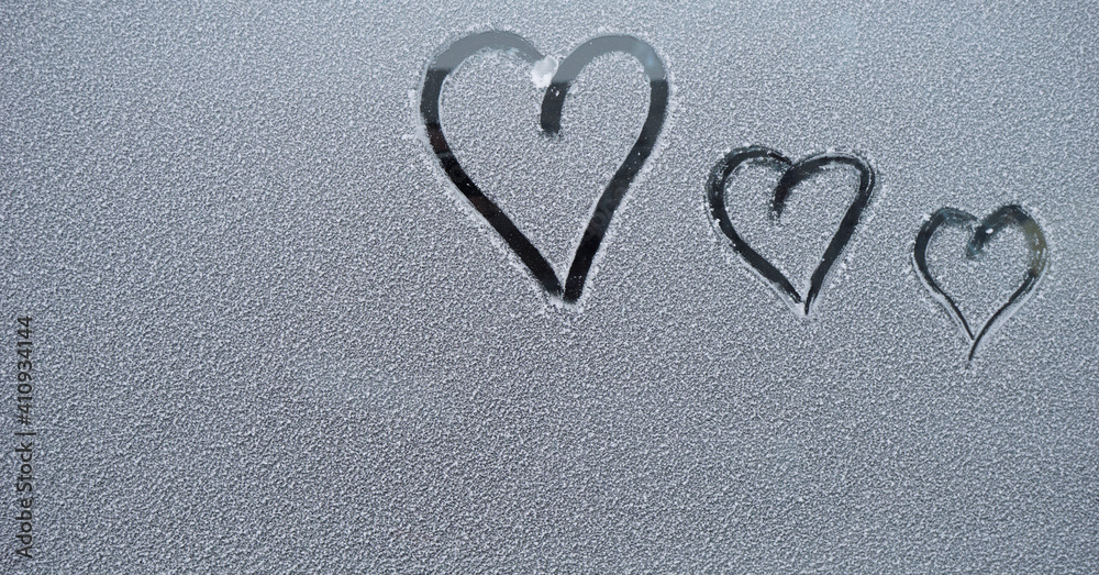three finger-drawn hearts on snow-covered glass   