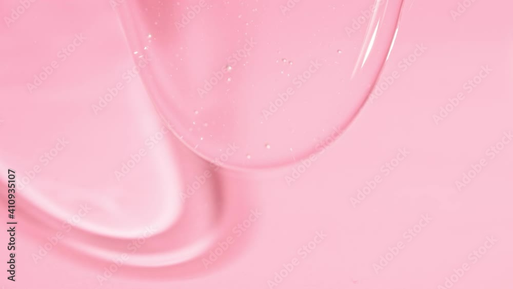 Transparent cosmetic liquid gel cream slowly drips flowing down on a pink background. Slime texture. 