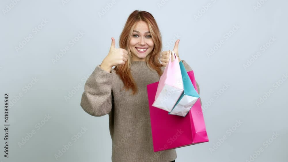 Teenager girl holding shopping bags giving thumbs up and smiling because something good has happened over isolated background Teenager girl holding shopping bags giving thumbs up and smiling because something good has happened over isolated background