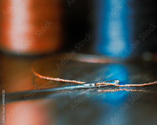 Threaded Needle on Table with Orange and Blue Spool in Background