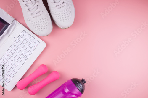 Online fitness. Sneakers, laptop, fitness bracelet, water bottle and dumbbells, on a pink background, workout online.