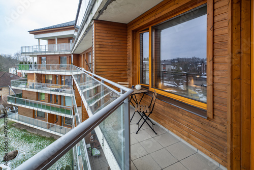 Wooden table and chairs on balcony in modern luxury apartment complex. View of winter city with green trees.