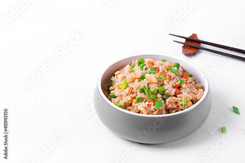 Fried rice with vegetables and egg in the gray ceramic bowl on the white table. Chinese food. Copy space