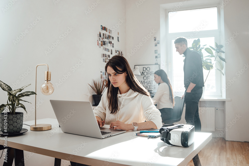 Concentrated beautiful woman in casual clothing works on her laptop in background of modern office and her collegues. Concentrated beautiful woman in casual clothing works on her laptop in background of modern office and her collegues.
