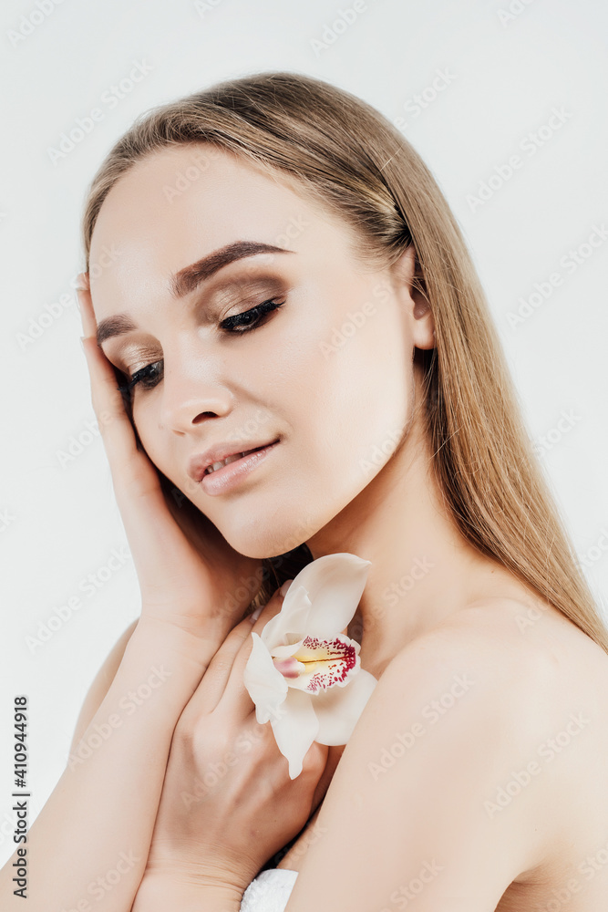 Portrait of an attractive blonde girl with radiant skin and a fresh orchid in her hand. Healthy facial skin. Natural