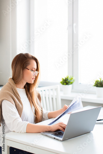 Online work concept. Vertical photo of a woman works online in front of a laptop monitor. She fills out tax forms or pays bills. Photo in home interior.