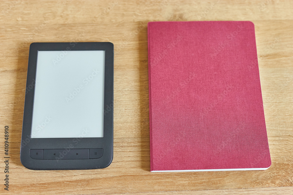 Close up shot of black electronic book with empty screen and red notepad on wooden table top view. Copy space for advertise text Close up shot of black electronic book with empty screen and red notepad on wooden table top view. Copy space for advertise text