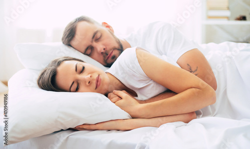Beautiful tender young couple sleeping in big white bed and have good dreaming.